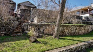 Un mur de soutènement en pierre, avec une zone herbeuse devant, un arbre et un bâtiment doté d’un balcon en arrière-plan.