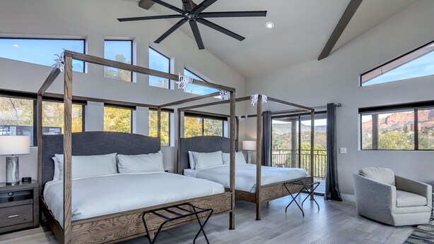 Een moderne slaapkamer met een hemelbed, een zithoek en grote ramen met uitzicht op het landschap.