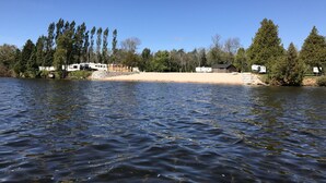 Un camping para vehículos recreativos a orillas de un lago, con varias caravanas estacionadas frente a la orilla, rodeado de árboles densos.