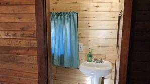 Un baño con paneles de madera, un lavamanos blanco, una cortina azul y un inodoro.