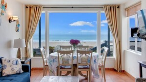 Una habitación con vista a la playa, una mesa de comedor con sillas, un sofá, una lámpara y un televisor.