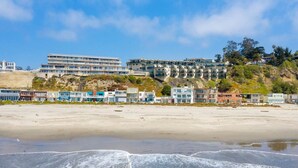 Un hotel frente al mar con varias edificaciones, una playa de arena y olas.