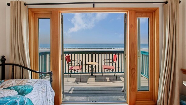 Una habitación con una cama, un balcón con mesa y sillas, y vista a la playa.