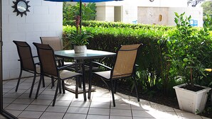 Une terrasse extérieure avec une table et des chaises, un parasol bleu et une horloge au mur.