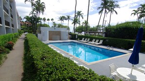 Une piscine entourée de verdure et de palmiers, avec des chaises longues et une table à proximité.