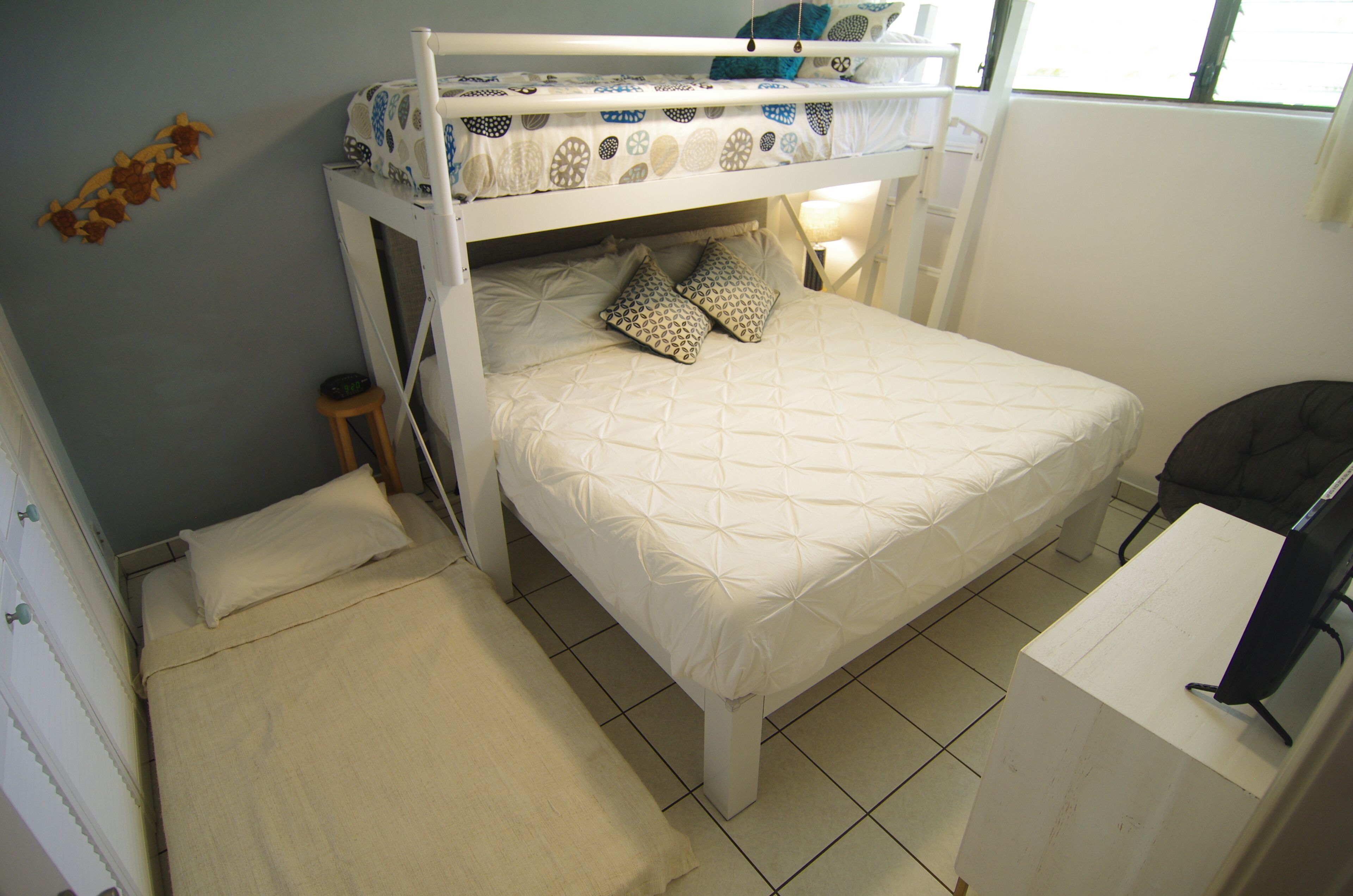 Un lit superposé avec un lit inférieur, une table de chevet, une lampe et un petit tabouret.