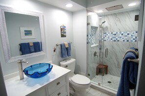 Une salle de bain avec un lavabo en verre, des toilettes, une douche avec une porte en verre et un mur de douche recouvert de carreaux.