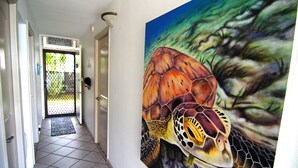 Un couloir orné d’une grande fresque représentant une tortue sur un mur, une porte portant l’inscription « AVENTURE » et un sol carrelé.