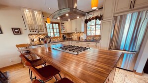 Una cocina moderna con una isla central, taburetes de bar, estufa y un refrigerador de acero inoxidable.