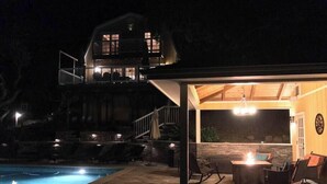 Una casa de dos pisos con un patio cubierto que tiene zona de estar exterior y una piscina.