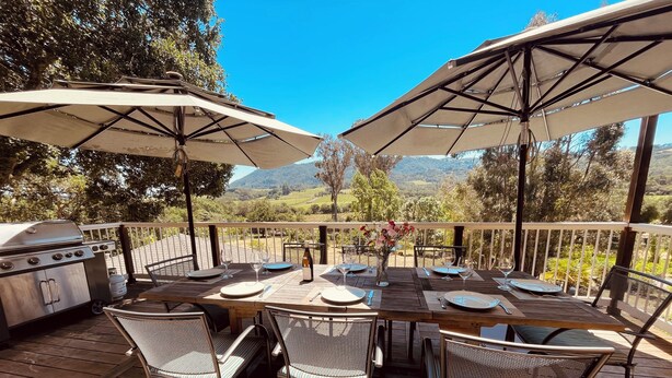 Un área de comedor al aire libre con terraza de madera, sillas de metal y sombrillas grandes.
