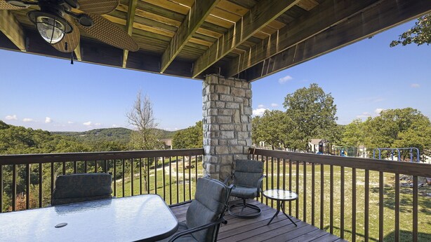 A wooden deck with a stone pillar, outdoor seating, and a view of a green landscape.