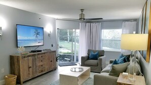 A living room with a television, a wooden cabinet, a coffee table, a sofa, and a lamp.