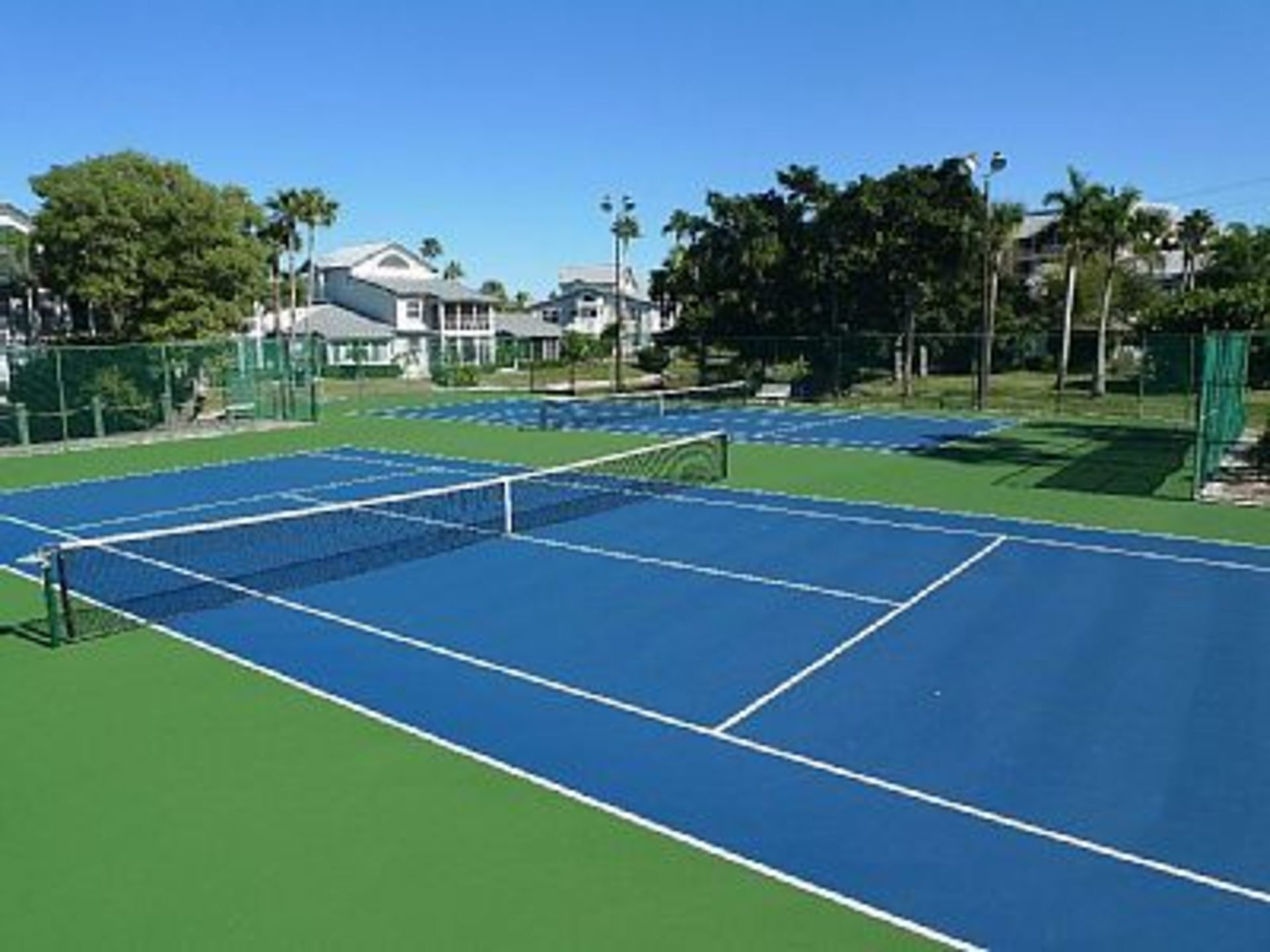 A tennis court with a net, surrounded by a fence and trees.
