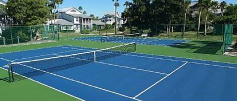 A tennis court with a net, surrounded by a fence and trees.