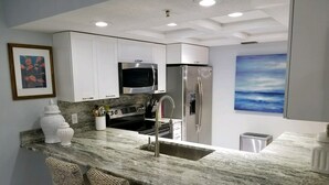 A modern kitchen with white cabinets, stainless steel appliances, a marble countertop, and wicker chairs.