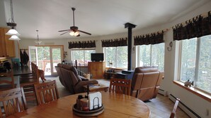 A spacious living room with a large wooden dining table, comfortable seating, a fireplace, and large windows offering a view of the outdoors. - Panoramic Views - Dog Friendly - Close to Breckenridge (Alma)