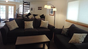 A living room with a dark-colored sofa set, a wooden coffee table, and a floor lamp. There is a staircase with a railing leading to an upper level. - Panoramic Views - Dog Friendly - Close to Breckenridge (Alma)