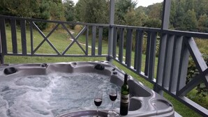 A hot tub with two glasses of wine and a bottle of wine on the edge.