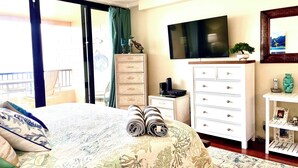 Een slaapkamer met een bed, dressoir, televisie en uitzicht op een balkon.