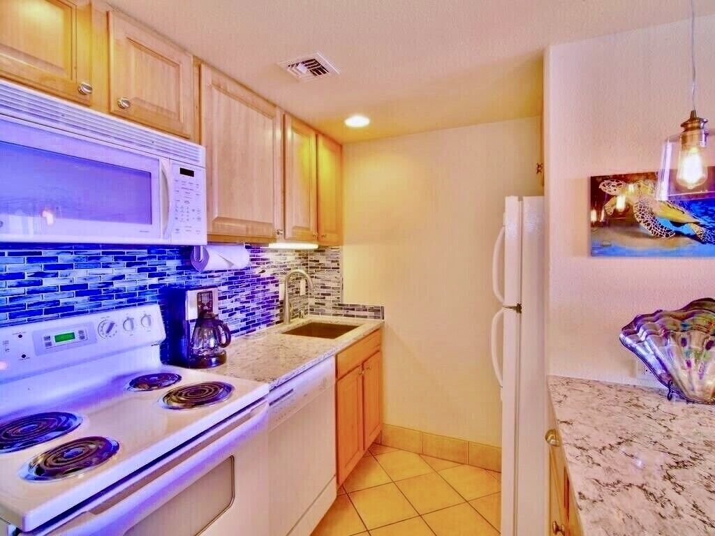 Una cocina con armarios de madera, un microondas, una estufa, un lavamanos y un refrigerador.