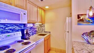 Una cocina con armarios de madera, un microondas, una estufa, un lavamanos y un refrigerador.