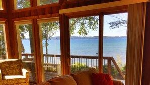Un salon confortable avec une grande fenêtre donnant sur un lac, aménagé avec un canapé et des fauteuils.