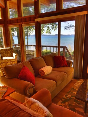 Relax in this inviting living room with a comfortable sofa, expansive windows, and a balcony overlooking a serene body of water.