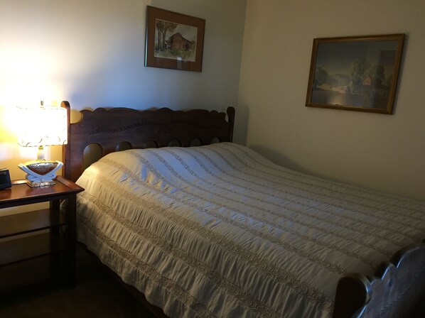 A neatly made bed with a patterned bedspread, a wooden headboard, a bedside table with a lamp, and two framed pictures on the wall.