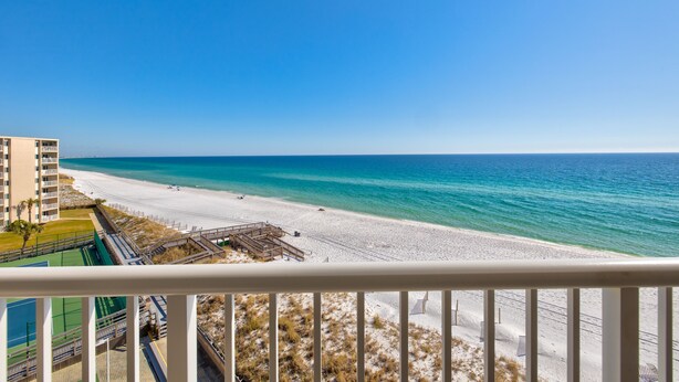 Blick auf einen Strand vom Balkon aus, mit blauem Himmel, Sandstrand und einem Gebäude im Hintergrund.