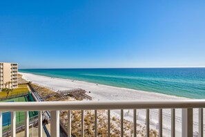 Une vue sur la plage depuis un balcon, avec un ciel dégagé, une plage de sable et un bâtiment en arrière-plan.