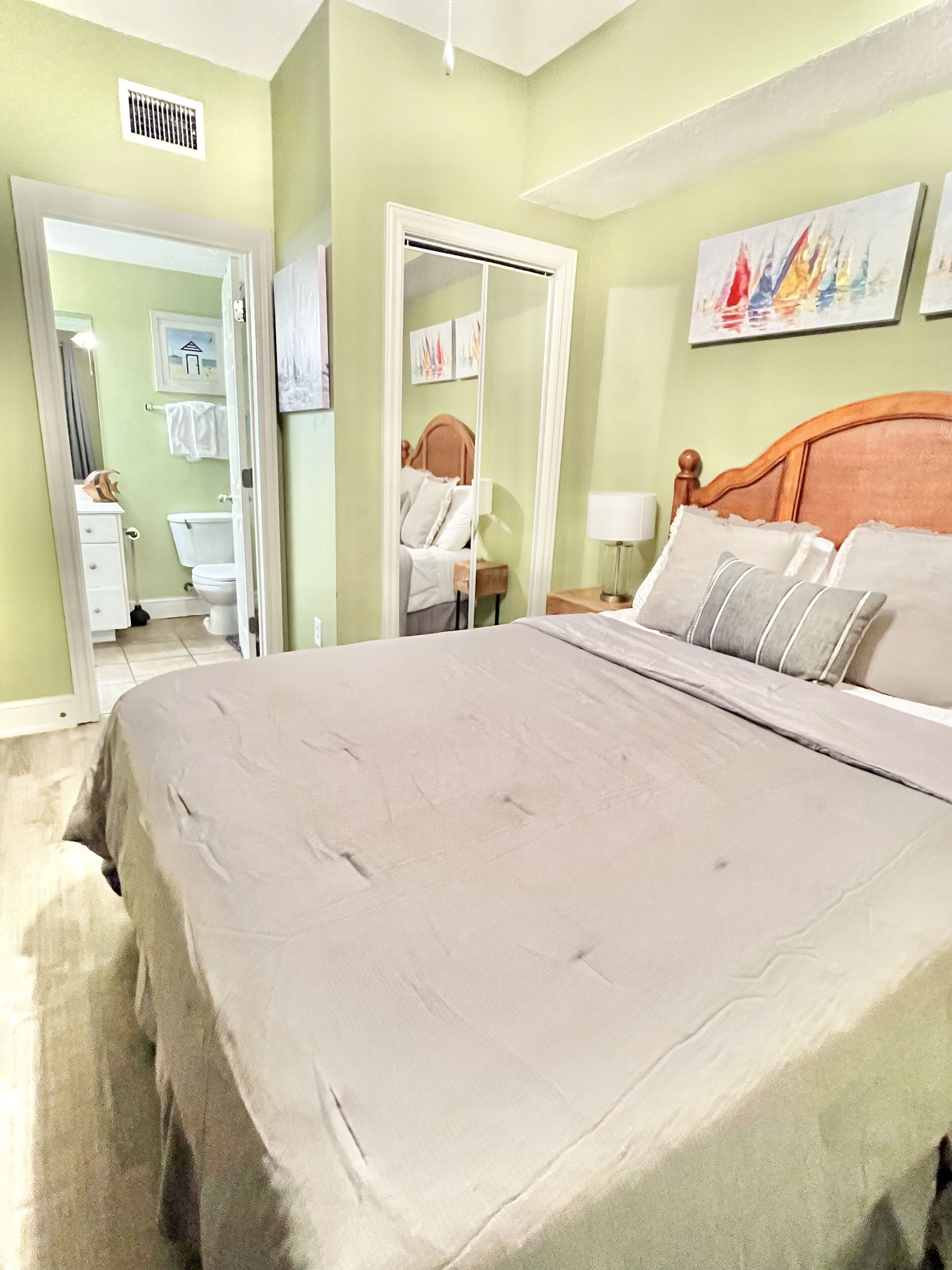 Un dormitorio con una cama grande, cabecera de madera, mesita de noche con lámpara y un cuadro en la pared.
