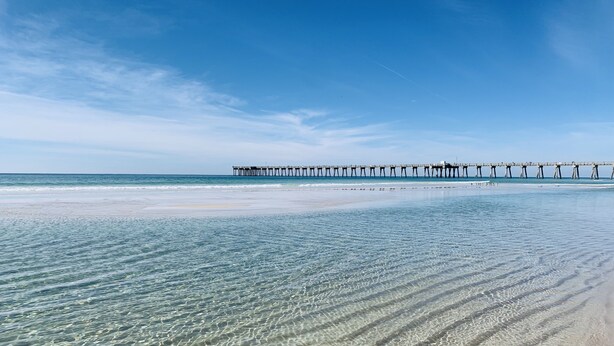 Une plage avec une eau claire et peu profonde, et une jetée qui s’avance dans l’océan.