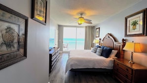 Une chambre d’hôtel avec un lit, une commode, un ventilateur de plafond et une vue sur l’océan, accessible par une porte coulissante.