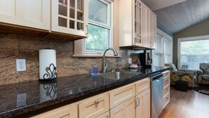 A kitchen with granite countertops, wooden cabinets, a stainless steel sink, and a window with blinds. - Historic Downtown │Walk Everywhere │Private Hot Tub │One Block to River (Bend)