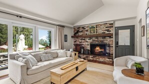 Un salon moderne avec une cheminée, un canapé, une table basse et une vue sur l’extérieur.