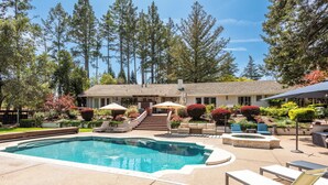 Un jardin avec une piscine, un espace salon extérieur et une maison avec un toit en tuiles.