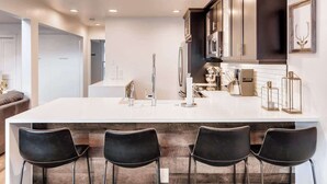 A modern kitchen with a large island, dark cabinets, stainless steel appliances, and a bar seating area. - True Ski/Golf-in,Ski-Out Luxury Modern with Views (Frisco)