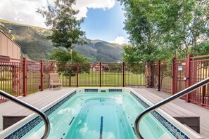 Piscina con vista a las montañas, rodeada por una cerca roja y una terraza con sillas.