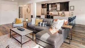 A modern living room with a grey sofa, a coffee table, and a kitchen area with dark cabinets and a microwave. - True Ski/Golf-in,Ski-Out Luxury Modern with Views (Frisco)