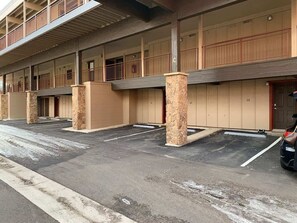 Un estacionamiento de varios pisos con pilares de piedra, una pasarela techada y la entrada a un edificio.