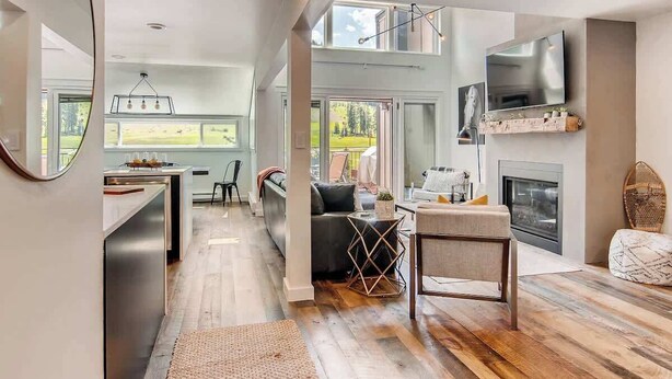 A spacious living area with a fireplace, a TV mounted on the wall, and a large window overlooking a garden. - True Ski/Golf-in,Ski-Out Luxury Modern with Views (Frisco)