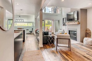 A spacious living area with a fireplace, a TV mounted on the wall, and a large window overlooking a garden. - True Ski/Golf-in,Ski-Out Luxury Modern with Views (Frisco)