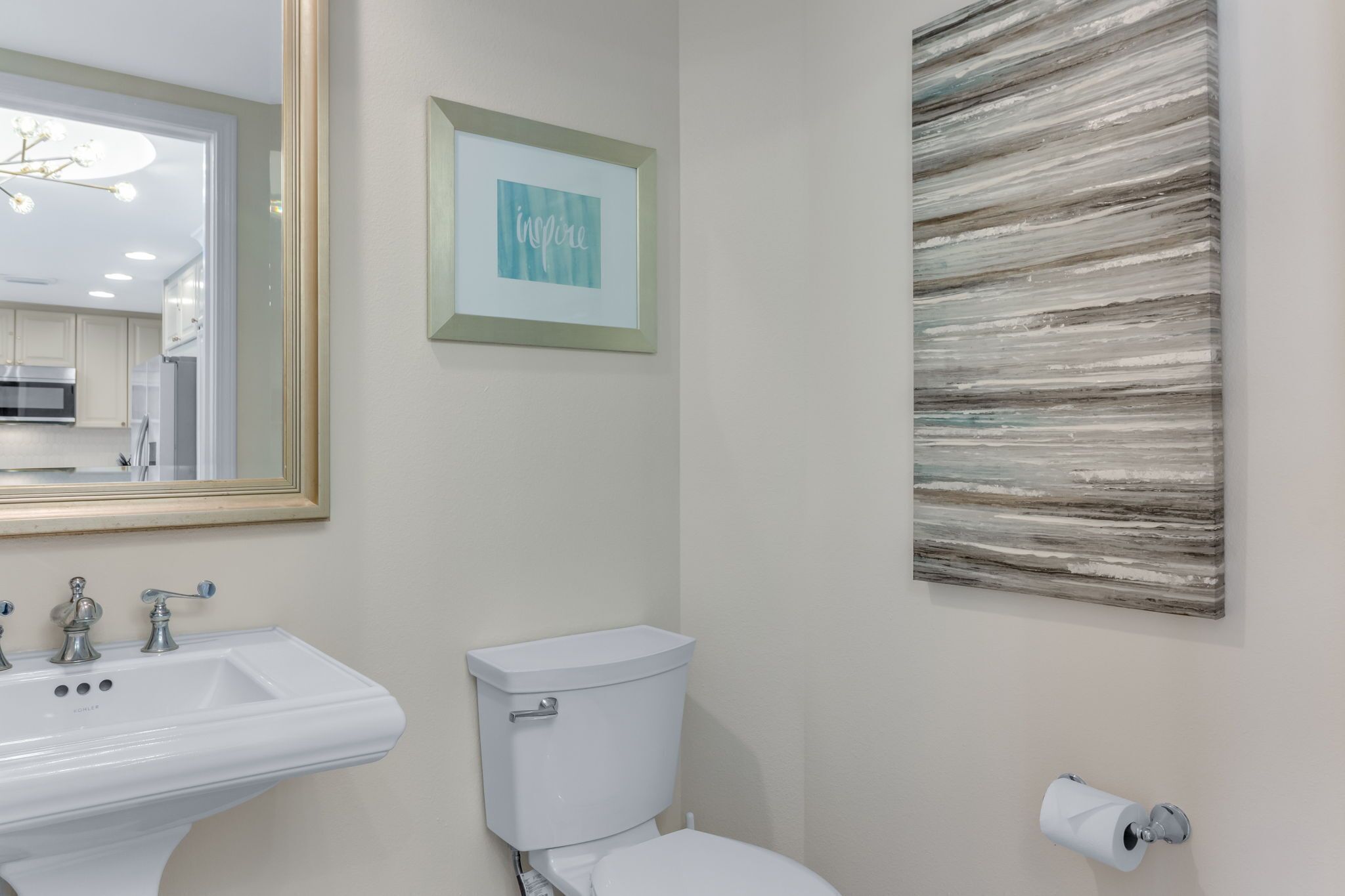 A bathroom with a sink, toilet, framed artwork, and a wall-mounted toilet paper holder.