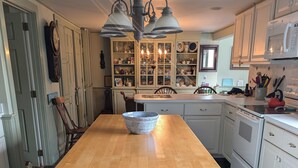 Une cuisine dotée d’un îlot central, de meubles blancs, d’un four à micro-ondes et d’un lustre.