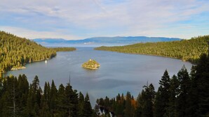 Un lago rodeado de un bosque tupido, con una pequeña isla en el centro y montañas al fondo.