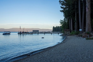 A calm lake with a wooden pier extending into the water, surrounded by trees and a distant mountain range. - Charming West Shore Chalet, Great Location, Close to the Lake, Hiking and Biking (Tahoma)