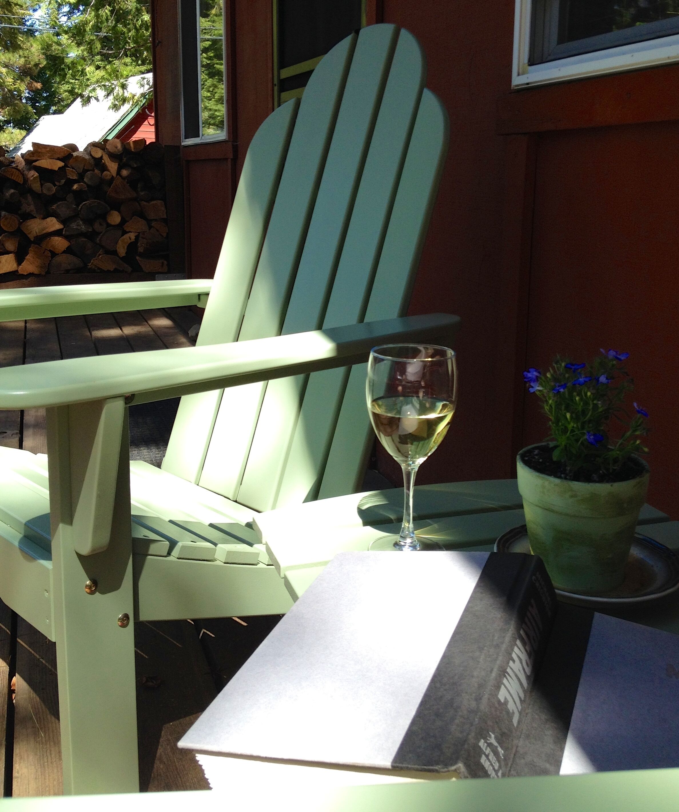 Ein grüner Adirondack-Stuhl mit einem Glas Weißwein und einem Blumentopf auf einem Tisch.