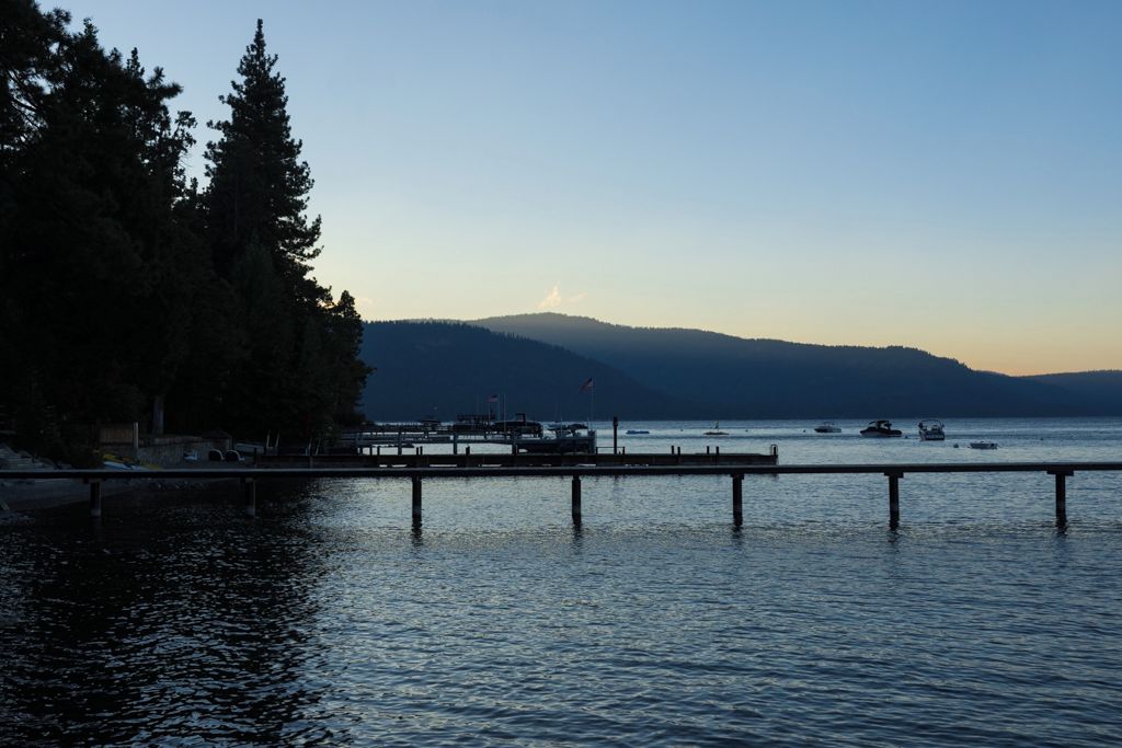 A waterfront view with a dock extending into calm water, surrounded by trees and a distant mountain range.