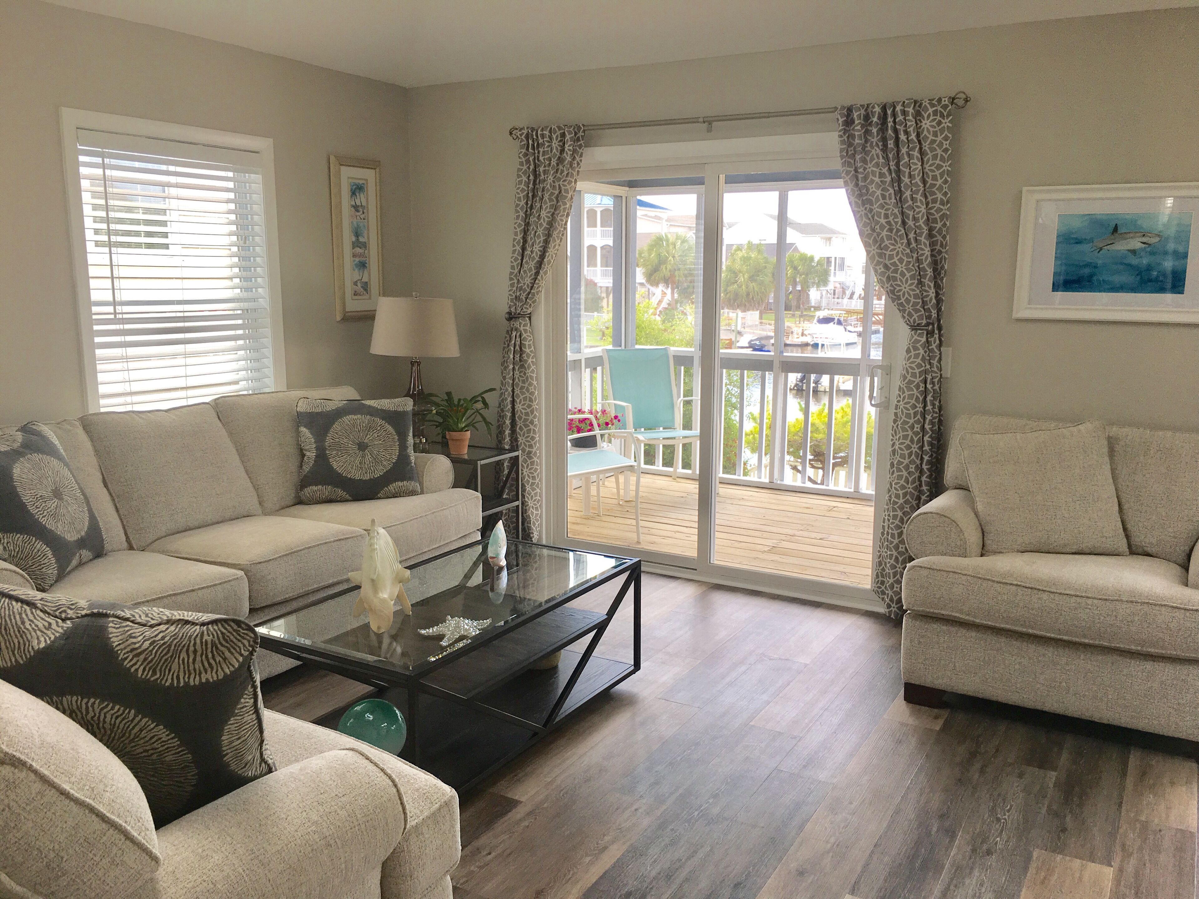 Een woonkamer met een bank, fauteuils, een salontafel en uitzicht op een balkon met buitenmeubilair.